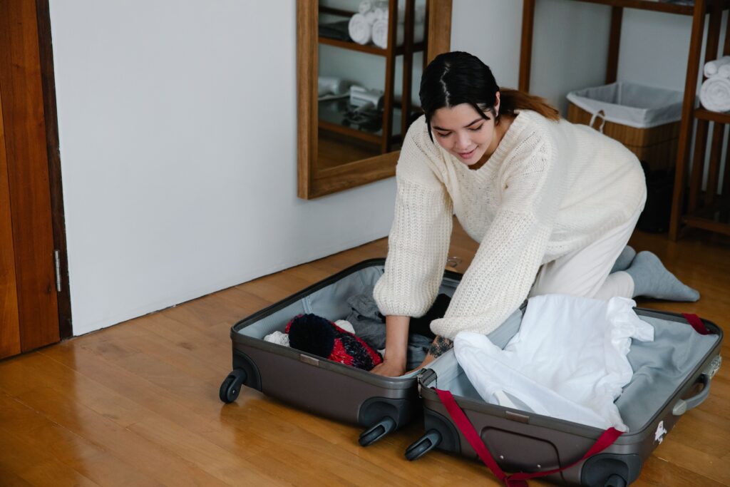 A student packing folded clothes into a suitcase in a bedroom before moving to university
