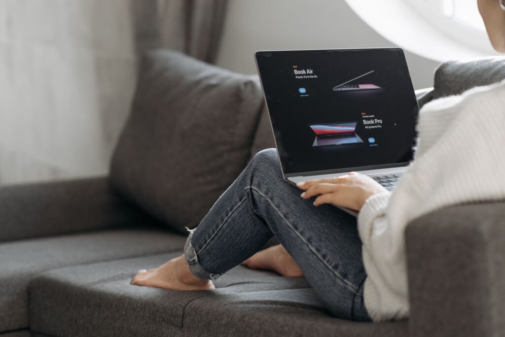 Woman sitting on a sofa comparing laptop listings on an online shopping site