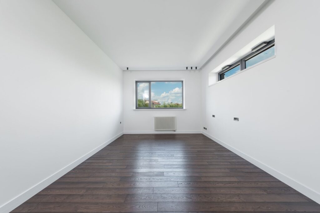 Empty unfurnished room with wooden flooring and a radiator under the window