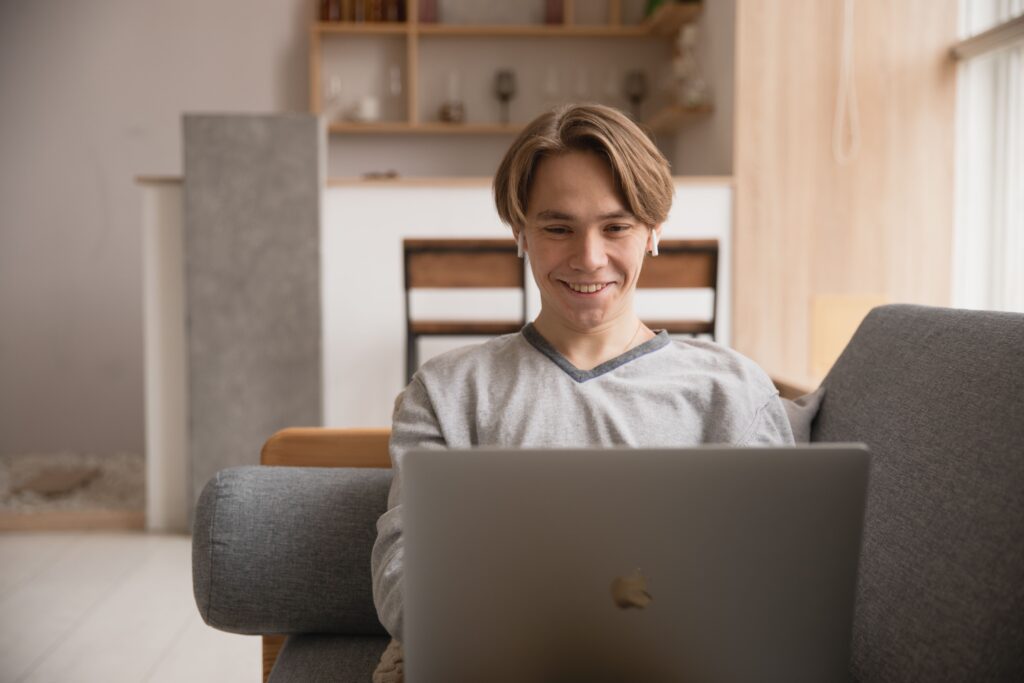 Young man smiling while using a laptop on a sofa at home