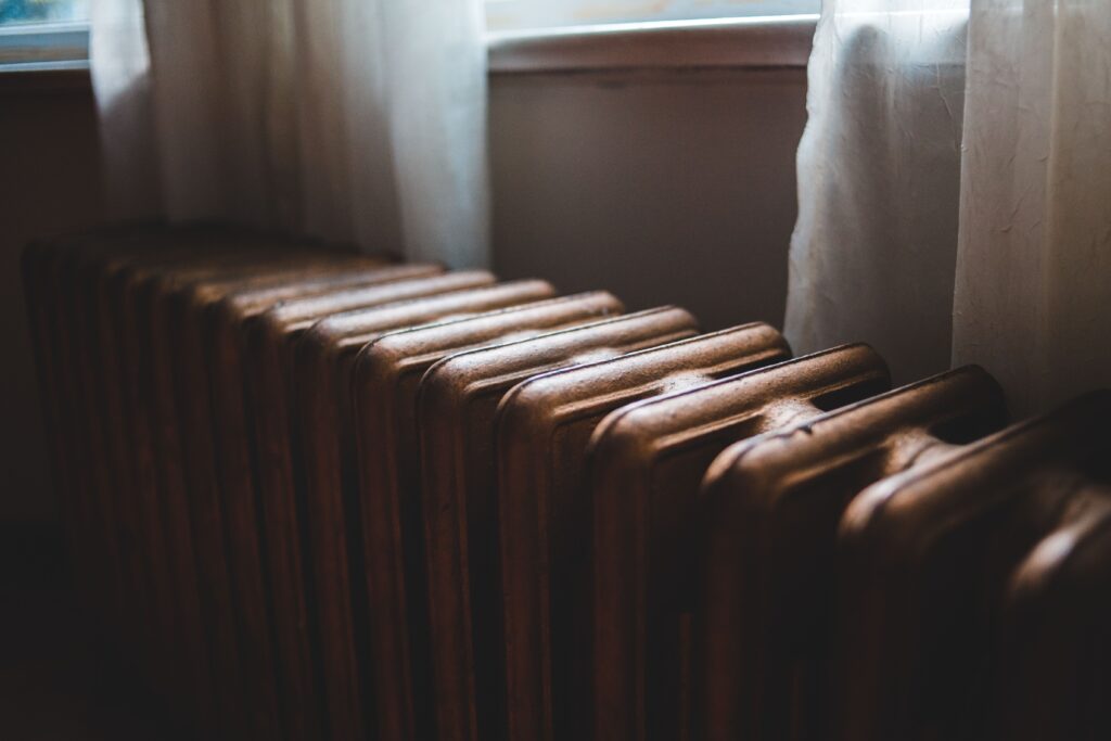 Old cast iron radiator below a window with net curtains