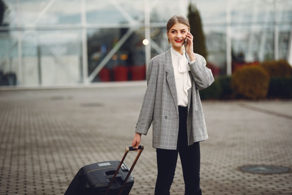 Young woman with a suitcase making a phone call outside an airport building