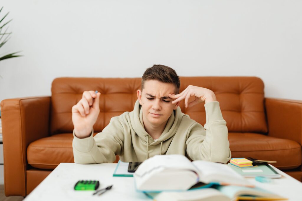 Teenage student frowning over books and notes at a table while weighing up his next step
