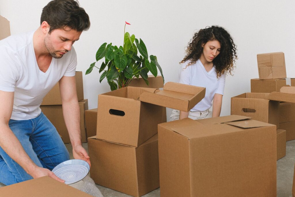 Two people wrapping plates and packing belongings into cardboard boxes for a move
