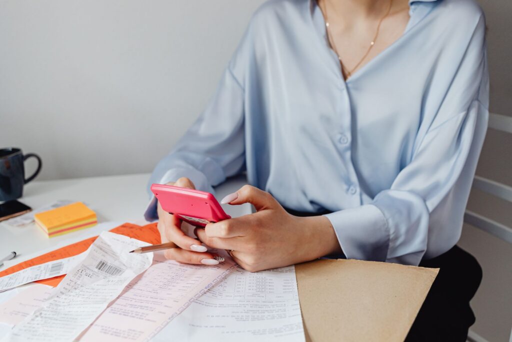 Person using a calculator to add up household bills and receipts at a table