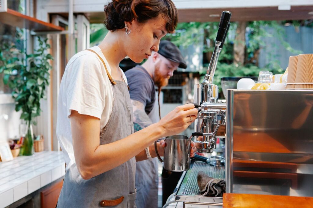 A student on a summer job shift steaming milk at a café espresso machine