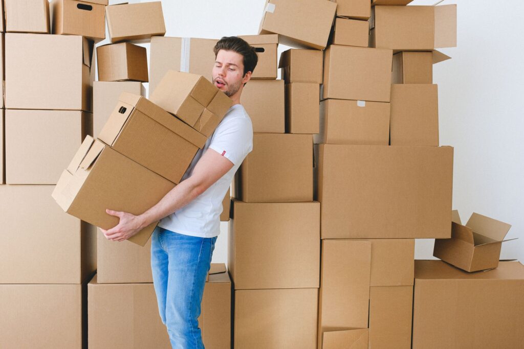 A student carrying a stack of cardboard moving boxes into a new place