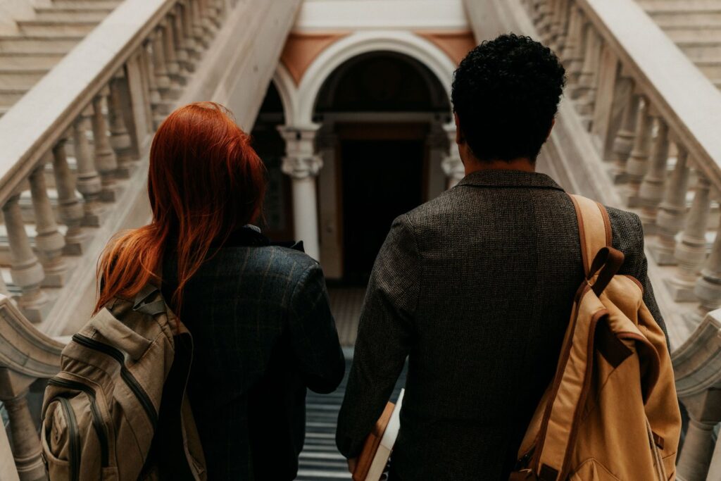 Two students with backpacks walking into a grand university building