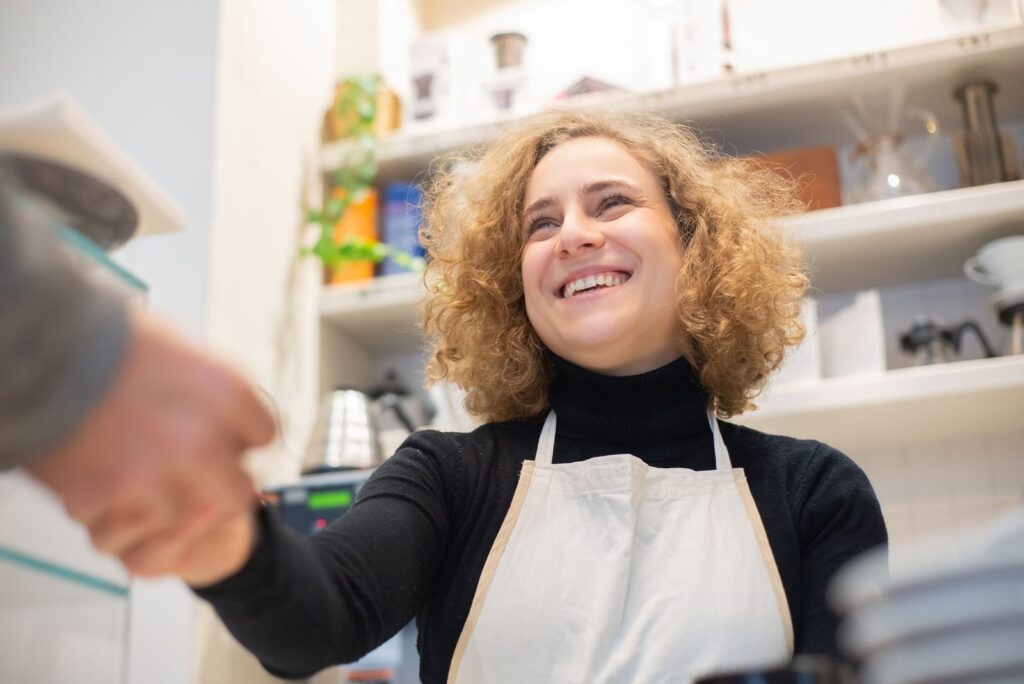 A young barista in an apron serves a customer at a coffee shop counter