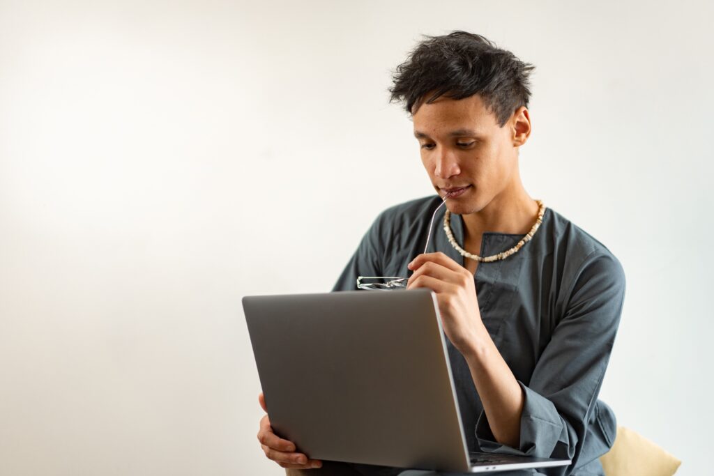 Young professional holding glasses and thinking while reading a laptop screen