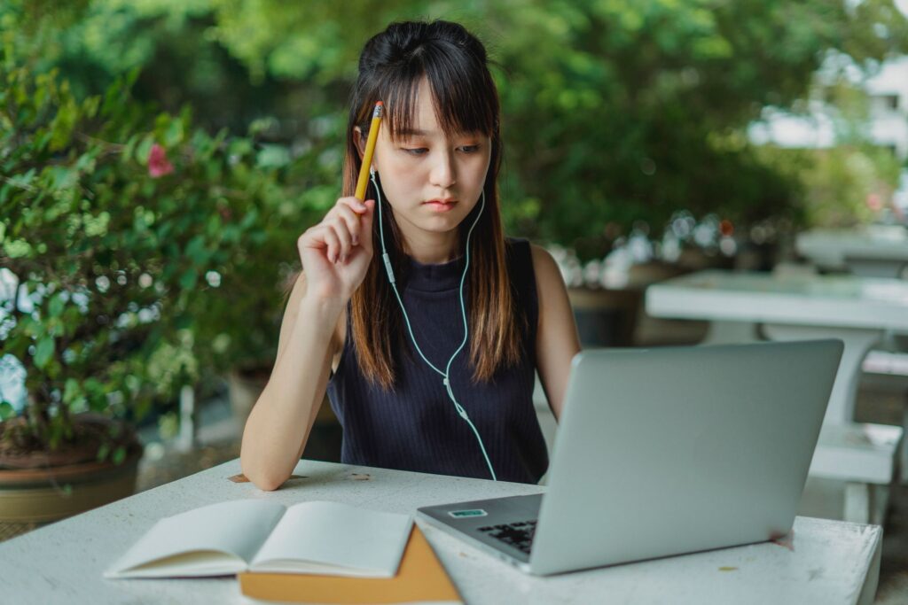 Student listening to an online lecture through earphones with a laptop and notebook