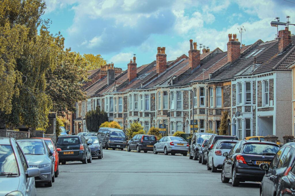 scenic view of parked cars along classic English townhouses under a blue sky.