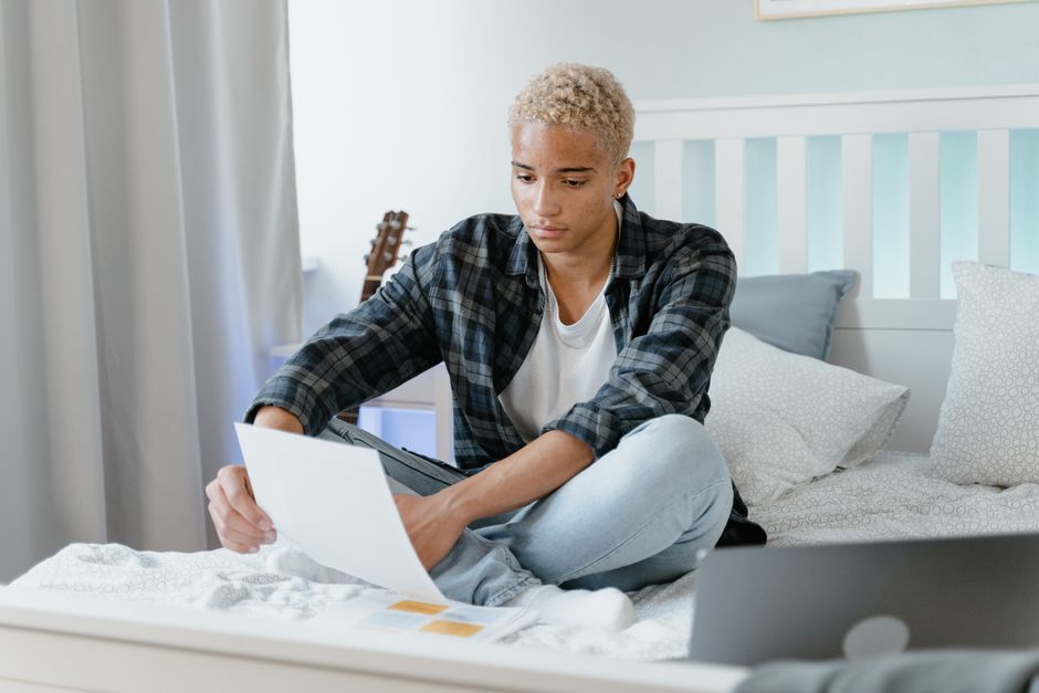 Student checking a maintenance loan letter on his bed beside a laptop