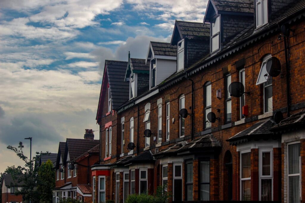 A row of red-brick Victorian terraced houses on a student street in Manchester, satellite dishes on the walls