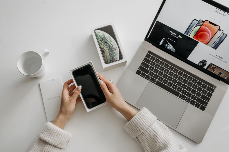 Unboxing a phone next to a laptop open on a tech retailer's page