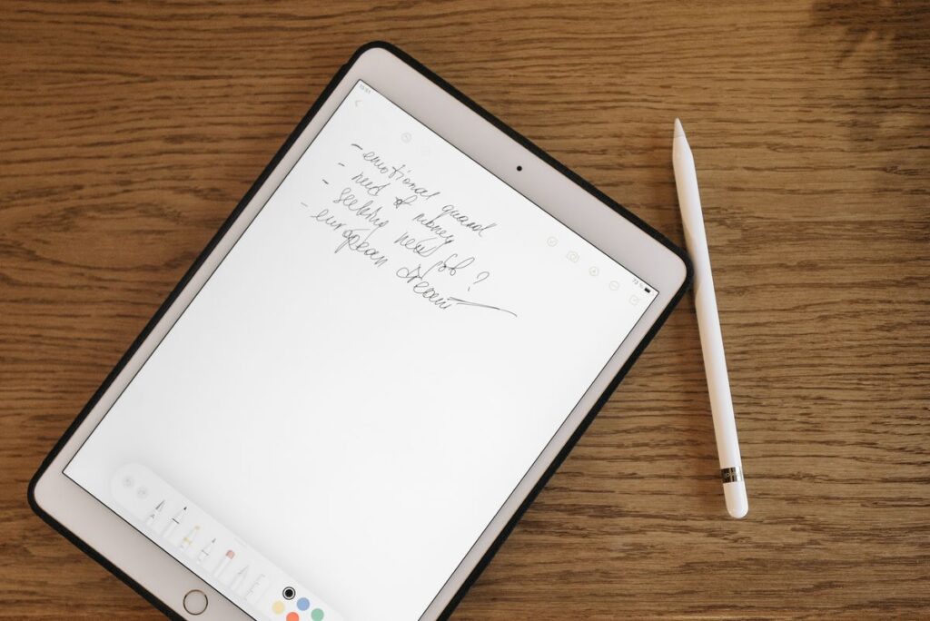 An iPad and Apple Pencil on a wooden desk, showing handwritten notes in a note-taking app