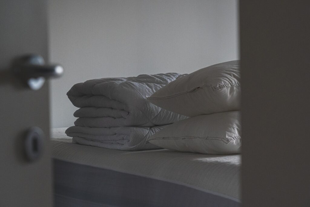 A folded duvet and two pillows stacked on a freshly made student bed