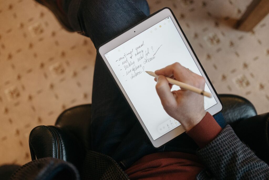 Student handwriting lecture notes on a tablet with a stylus while sitting in an armchair