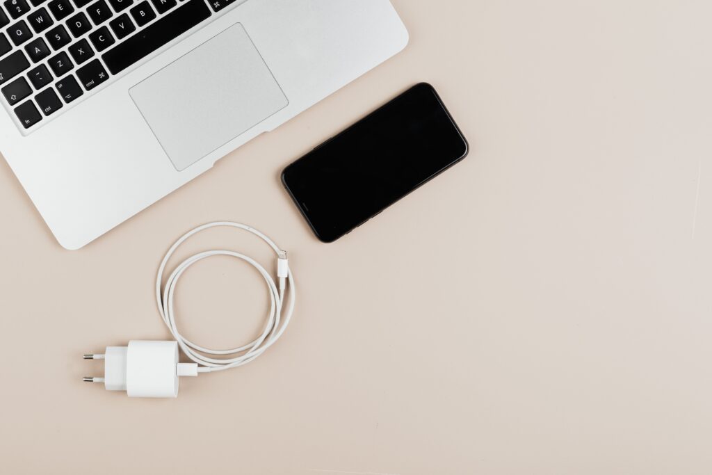 A laptop, phone and a coiled white charging cable with a plug on a desk