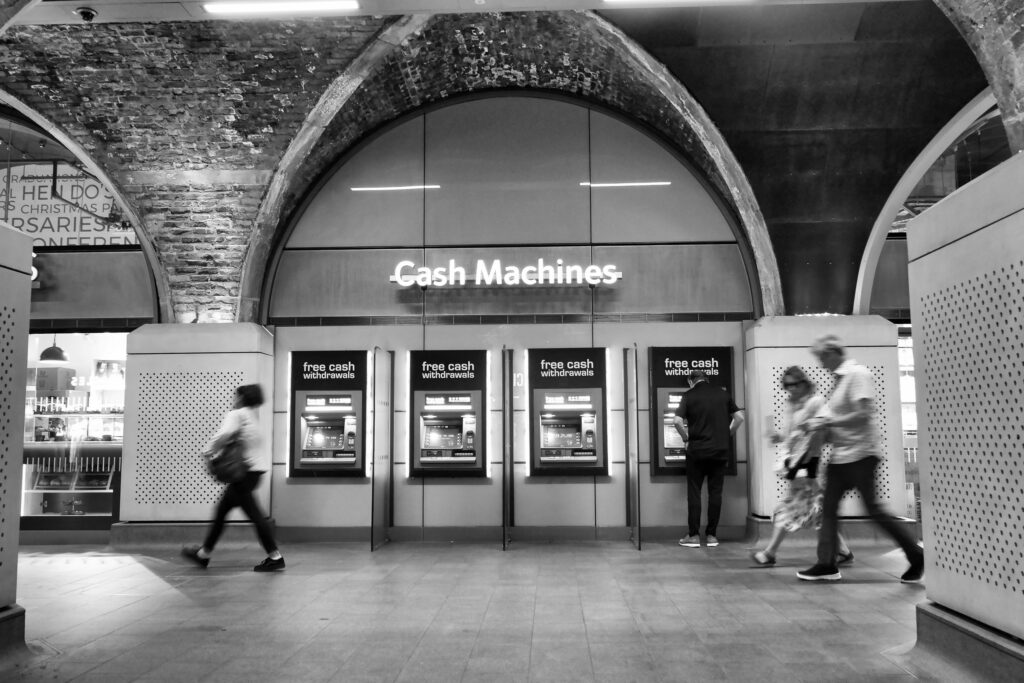 People using a row of free cash machines under brick railway arches, in black and white