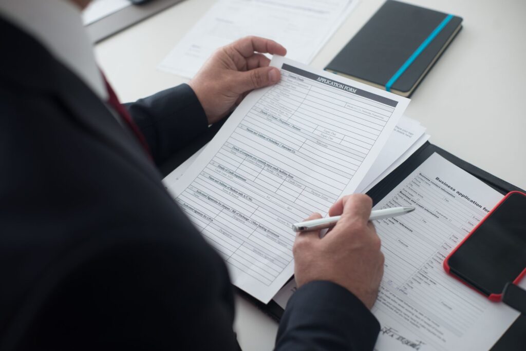 A recruiter holding a printed graduate application form and a pen, with more forms on the desk