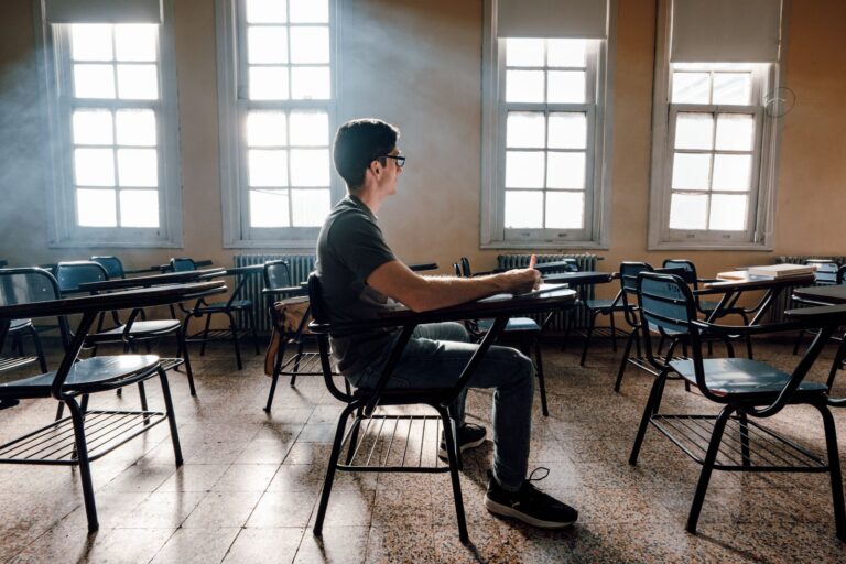 A student sits alone in an empty lecture room, looking out of the window