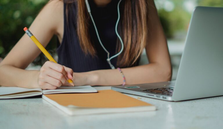 A graduate applicant drafts application form answers in a notebook beside a laptop