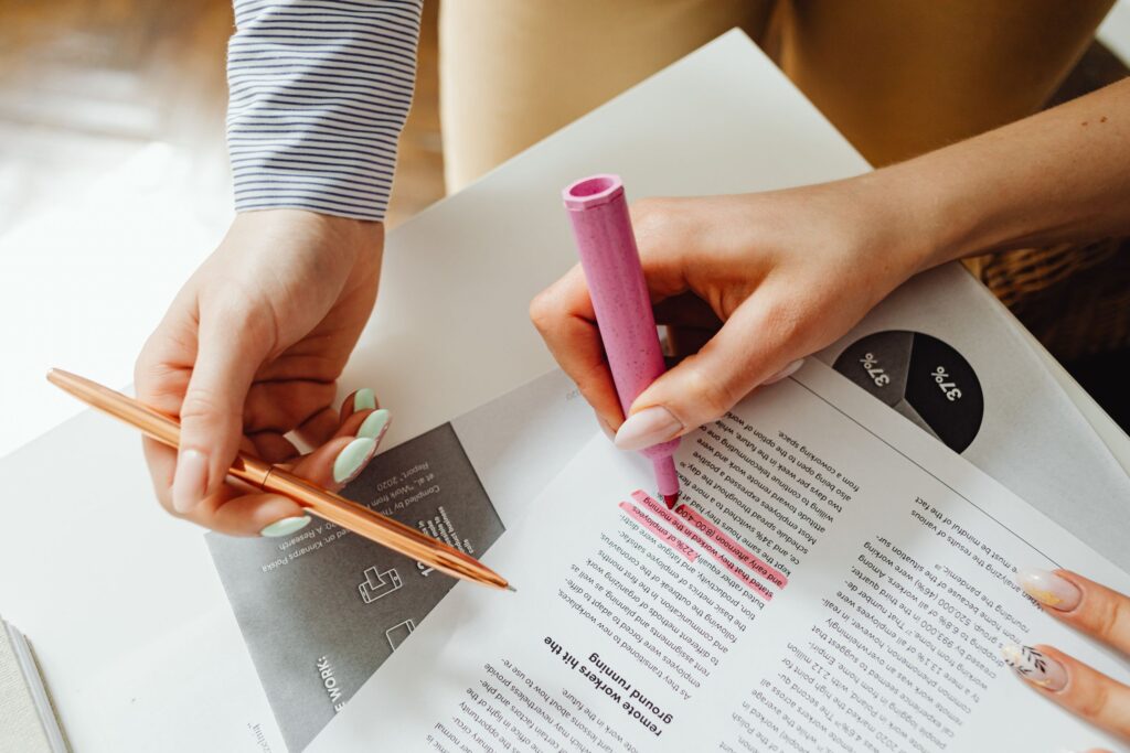 Hands with a pink highlighter and a pen marking lines on a printed report