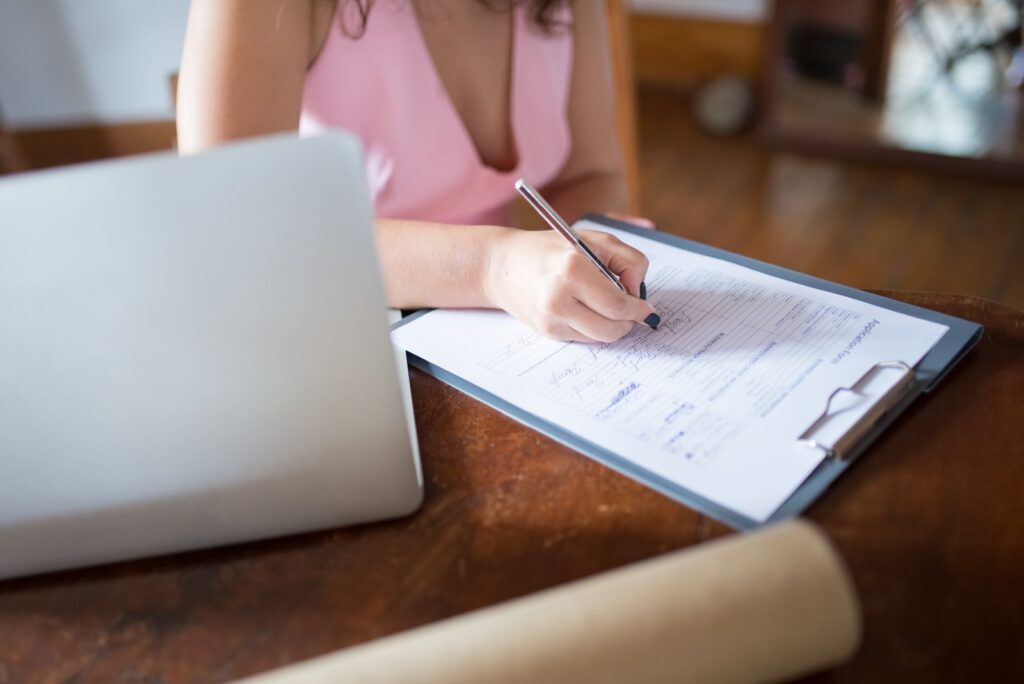 A student fills in a paper form beside a laptop, like the evidence letter for an extra year of student finance